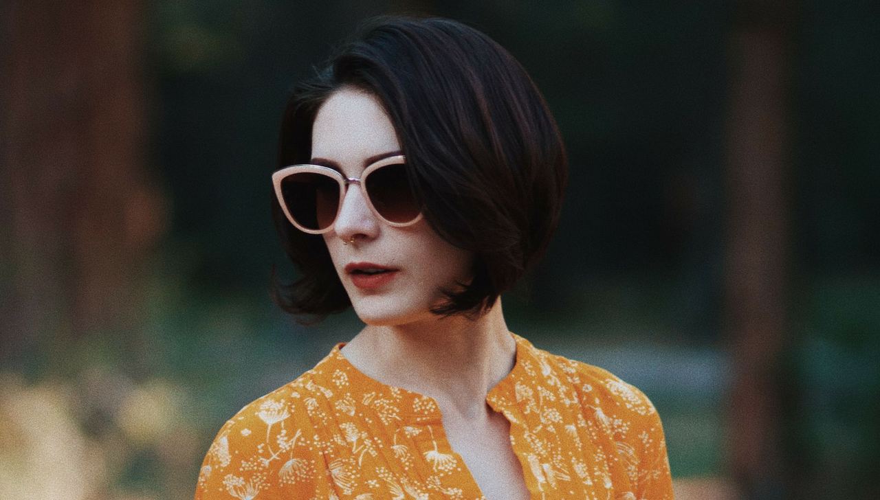 A woman in cat-eye sunglasses with pink lenses, in a floral orange blouse